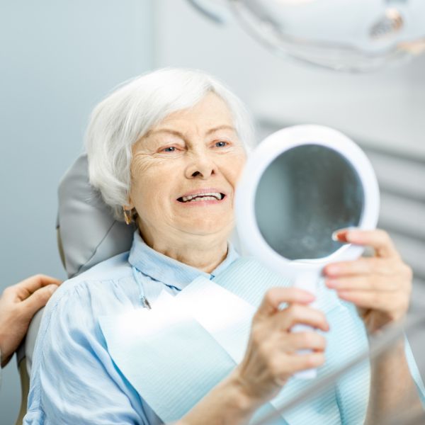 Older woman smiling as she checks her teeth in a hand mirror