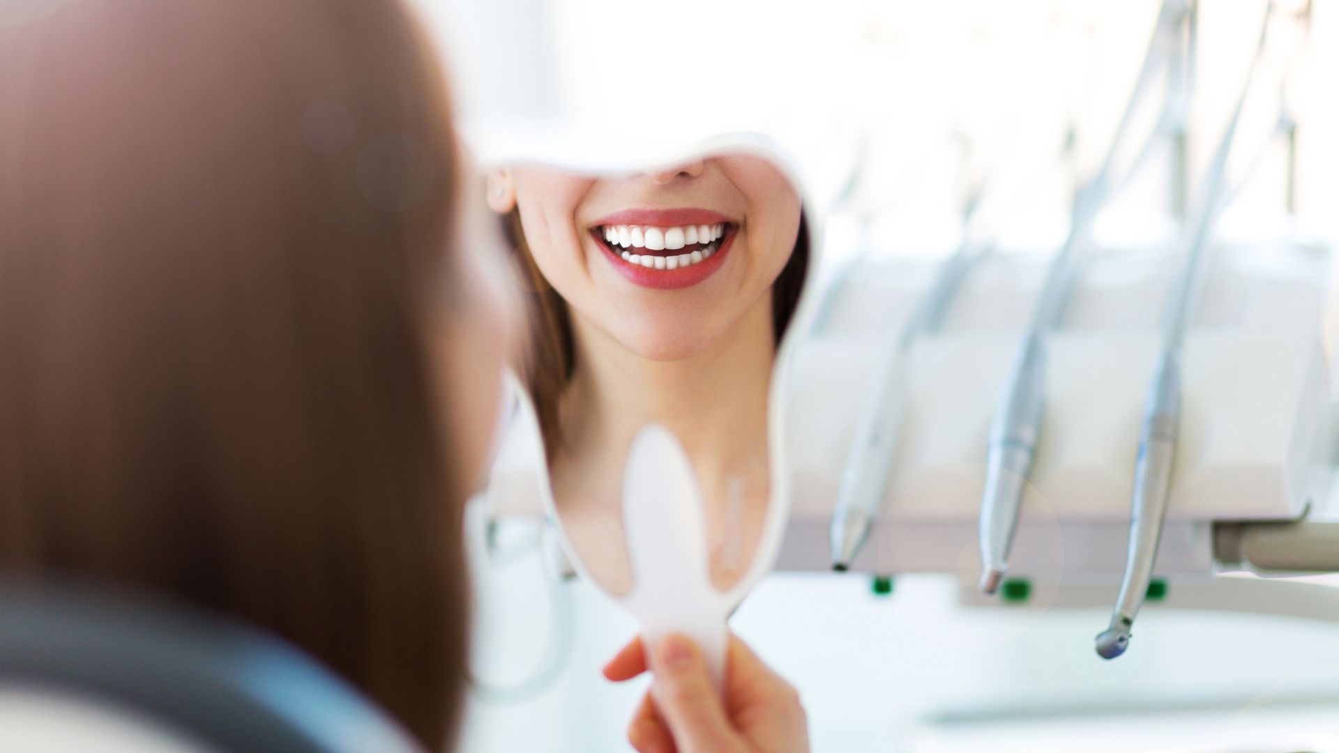 Woman smiling, holding mirror in dental office.