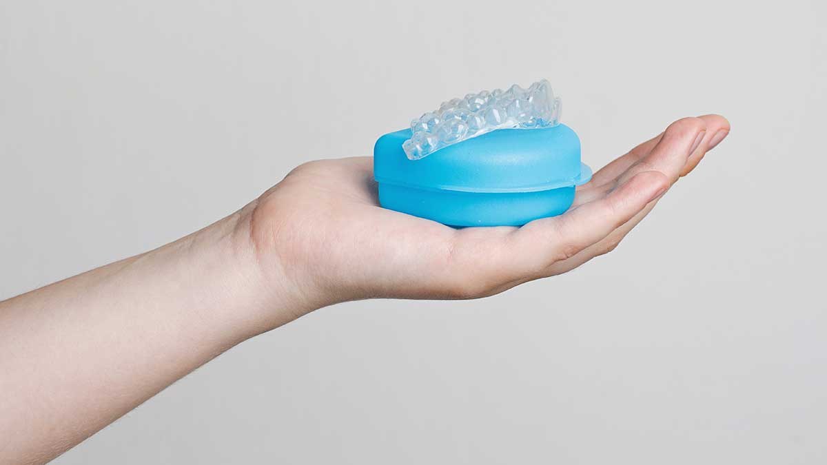 Clear aligner tray resting on a blue storage case held in an open hand