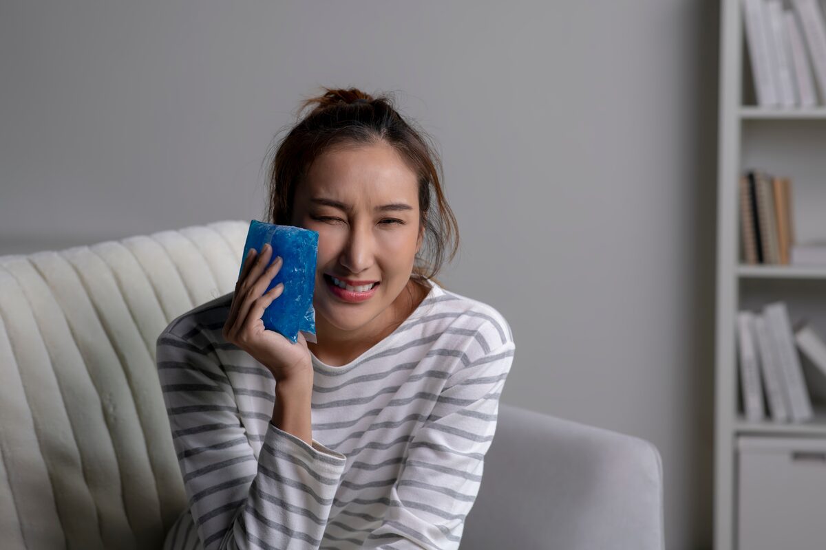 Woman sitting at home holding a cold pack against her cheek to ease tooth pain